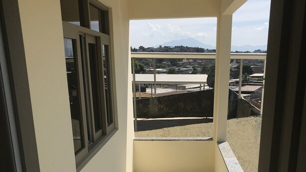 Ein enger Korridor mit einem Fenster, das auf einen Balkon mit Blick auf Gebäude und Berge führt.