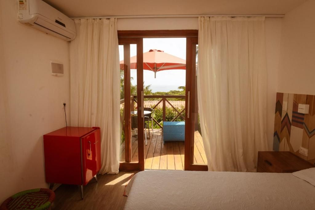 Et hotelværelse med en seng, et rødt skab, et vindue med gardiner og udsigt til et udendørs område med et bord og en parasol.