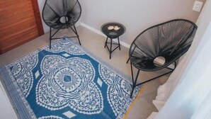 Une petite pièce avec un tapis à motifs, deux chaises noires, une petite table et une porte en bois.