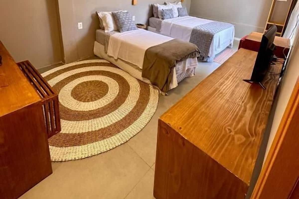 Een kleine slaapkamer met twee bedden, een houten bureau, een spiegel en een rond tapijt.