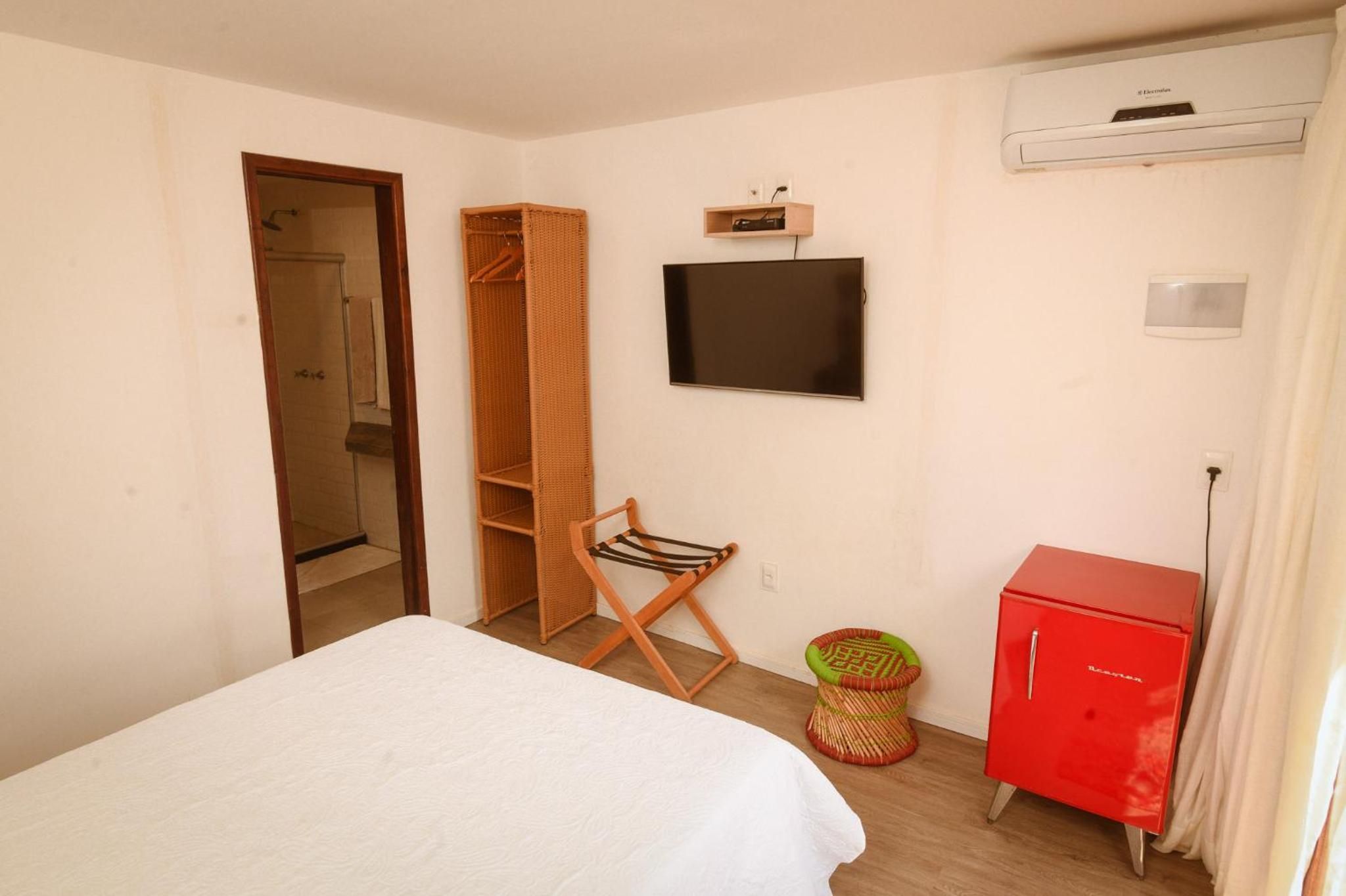 A bedroom with a bed, a television mounted on the wall, a wardrobe, and a red cabinet.
