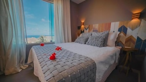 Une chambre avec un grand lit, une vue sur la mer et un mur orné d’un motif géométrique.