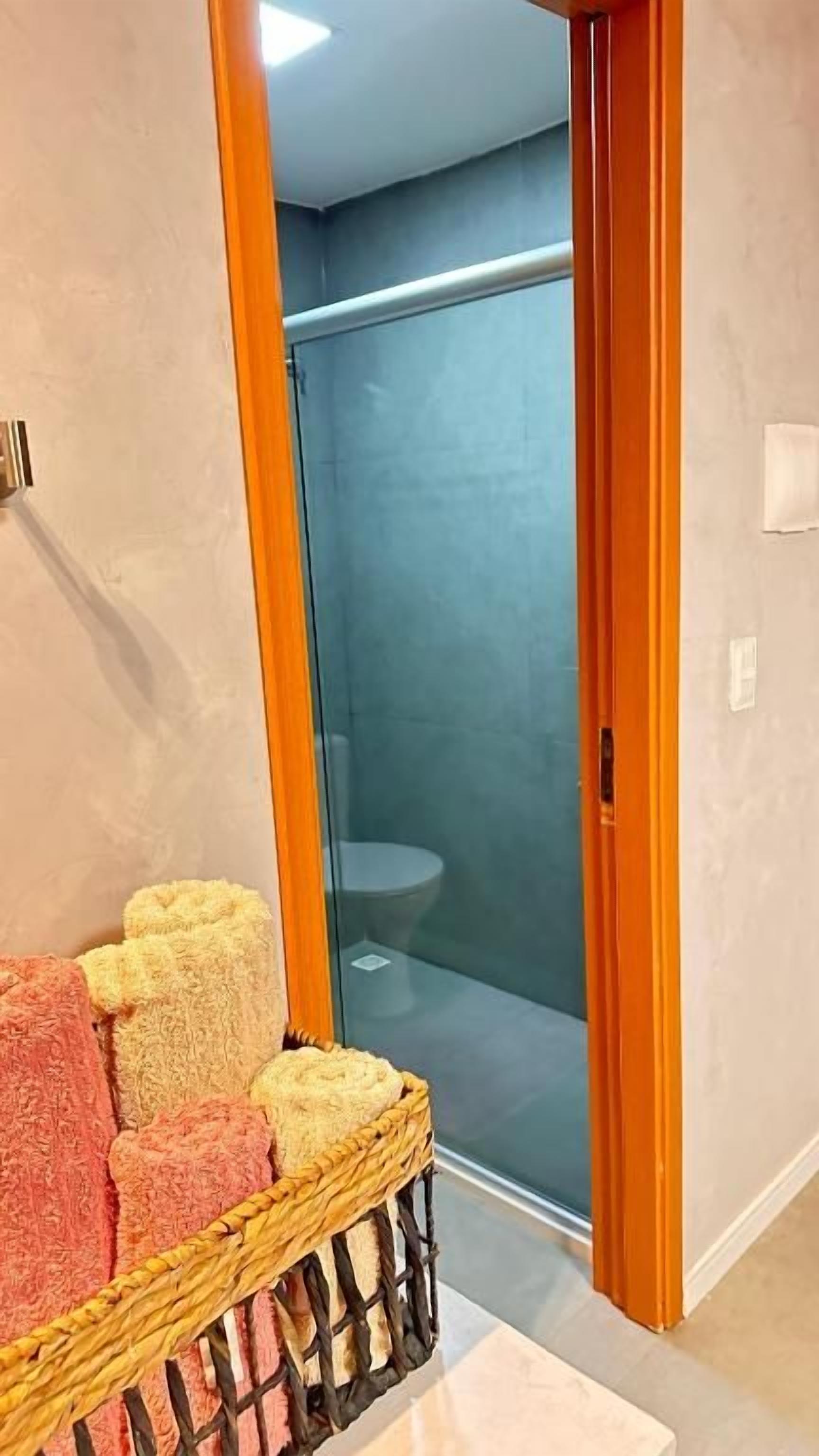A bathroom with a glass shower enclosure, a wicker basket with towels, and a wooden door frame.