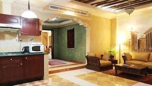 A hotel room with a kitchen area, a living room with a sofa and armchairs, and a dining area with a table and chairs. - ORIENTAL PALACE HOTEL APARTMENT (Dubai)