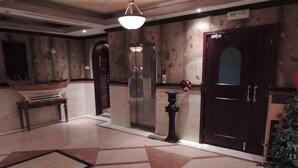 A lobby with a marble floor, a wooden bench, a ship model, a wall clock, and an elevator. - ORIENTAL PALACE HOTEL APARTMENT (Dubai)