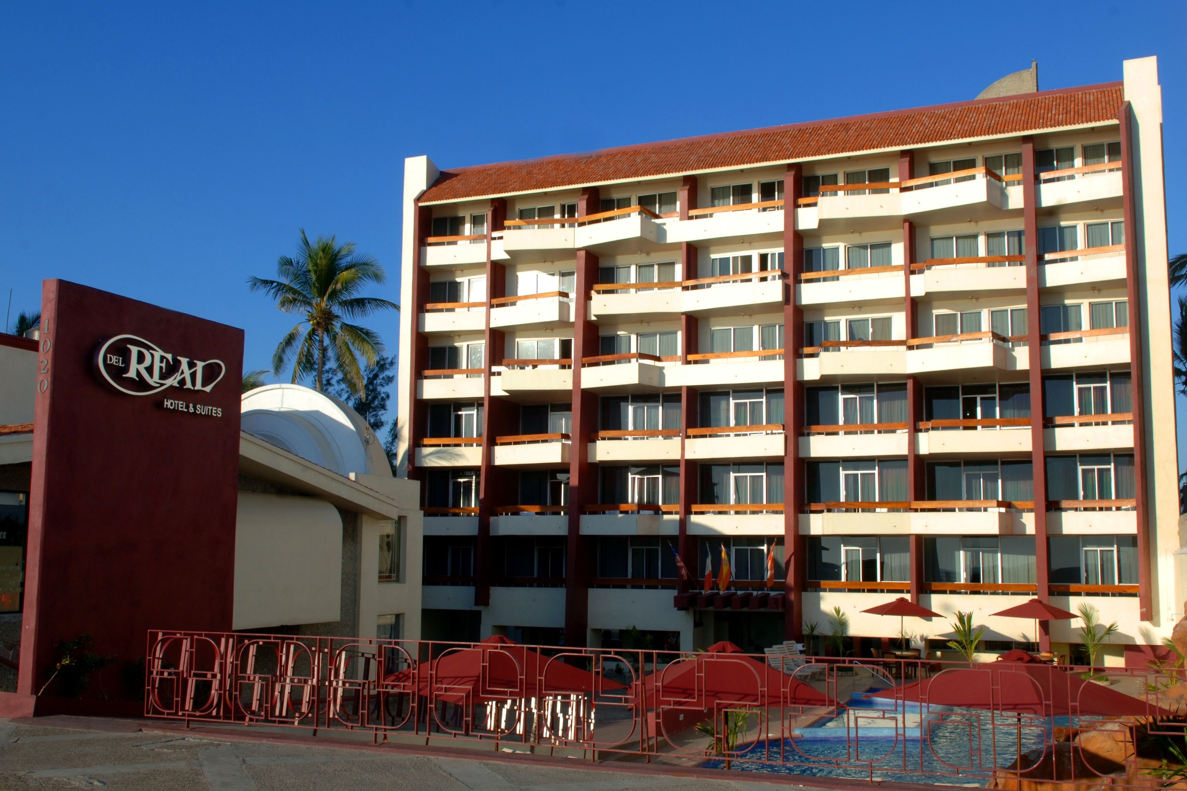 A multi-story hotel with a red and white facade, balconies, and a swimming pool area.