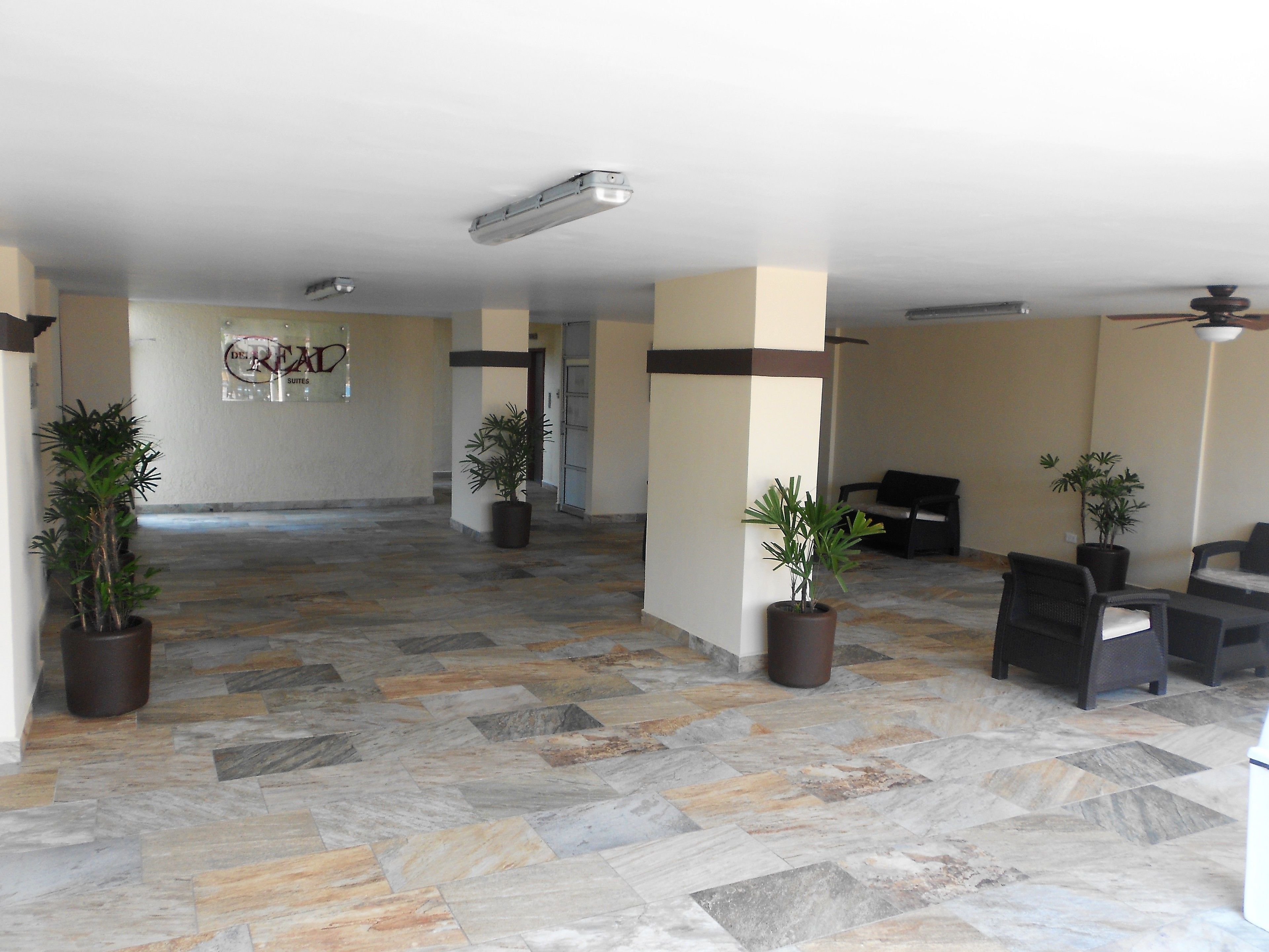 A spacious lobby with a tiled floor, potted plants, and a seating area.
