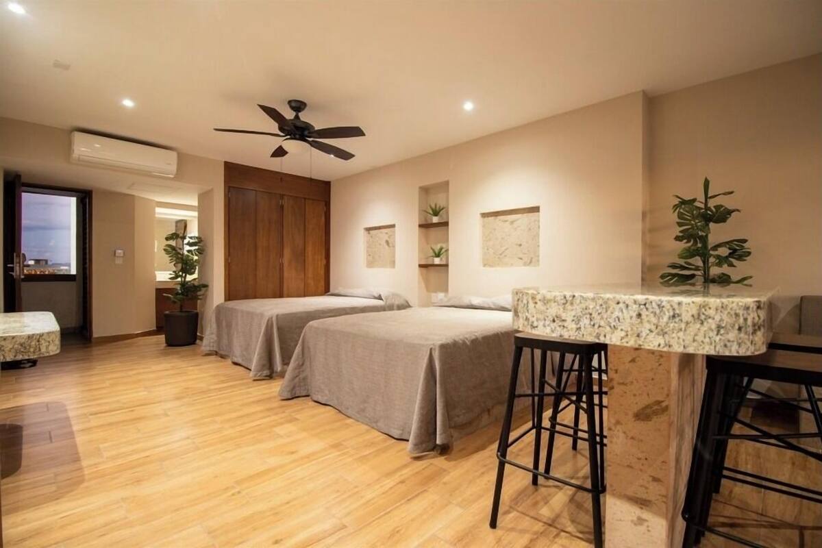 A hotel room with two beds, a ceiling fan, a small table, and a bar stool.