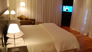Una habitación de hotel con una cama grande, un sofá, un televisor y una lámpara.