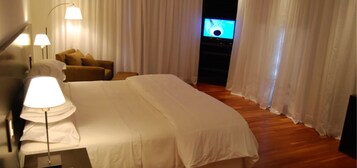 Una habitación de hotel con una cama grande, un sofá, un televisor y una lámpara.