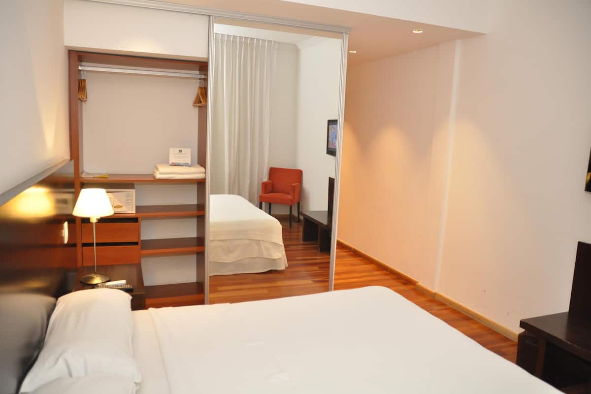 A hotel room with a bed, a desk, a chair, and a wardrobe.