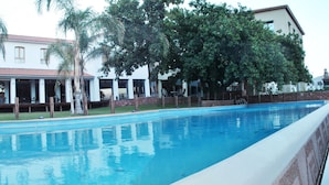 Una piscina con borde de baldosas, rodeada de palmeras y un edificio con techo de tejas.