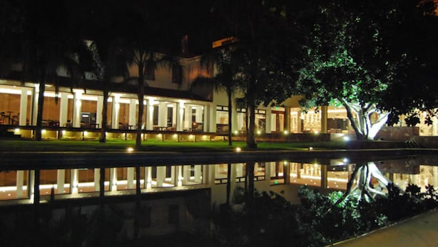 Un edificio con una piscina reflectante en primer plano, iluminado por luces.