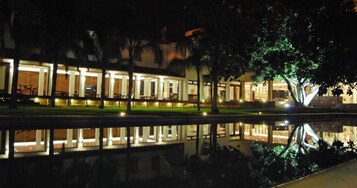 Un edificio con una piscina reflectante en primer plano, iluminado por luces.