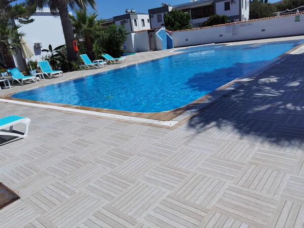 Piscina con agua azul, rodeada por un solárium con baldosas y sillas de descanso.