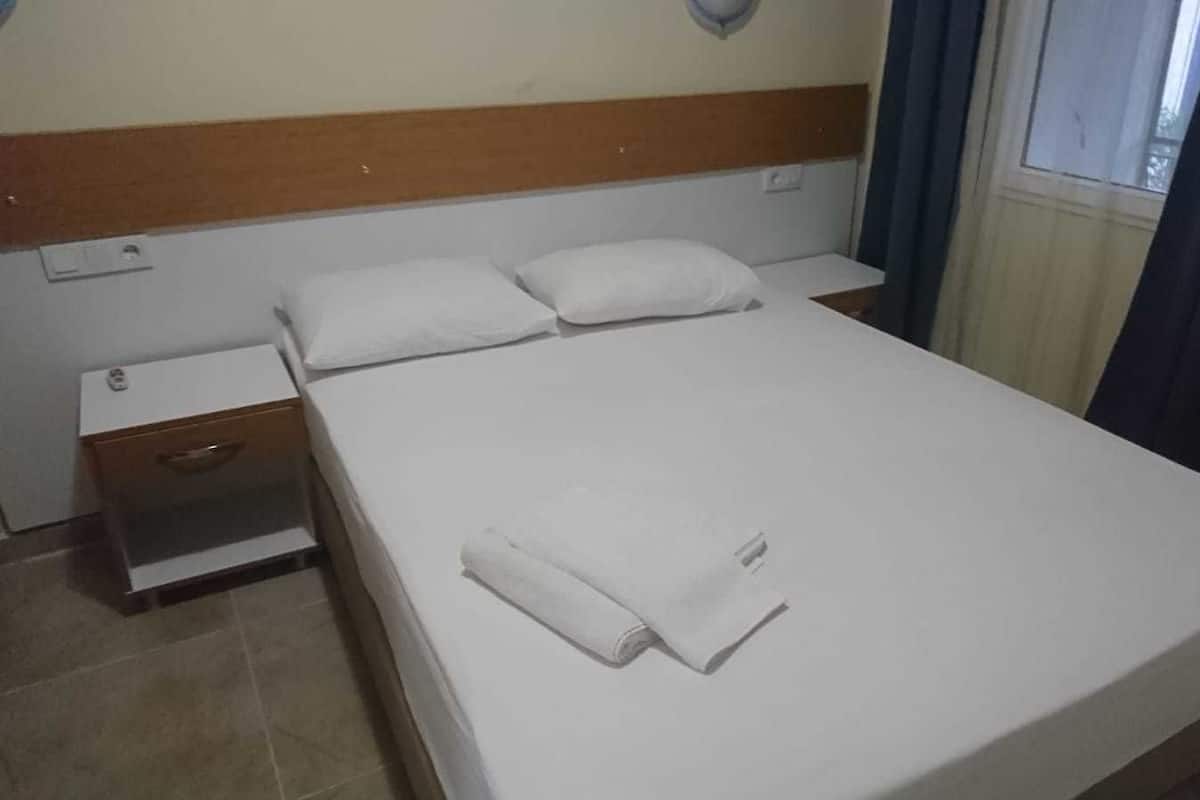 A hotel room with a single bed, a wooden headboard, a nightstand, and a window with curtains.