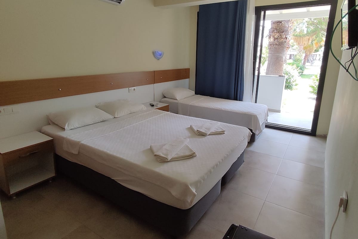 A hotel room with two beds, a ceiling fan, an air conditioning unit, and a view of the outdoors.