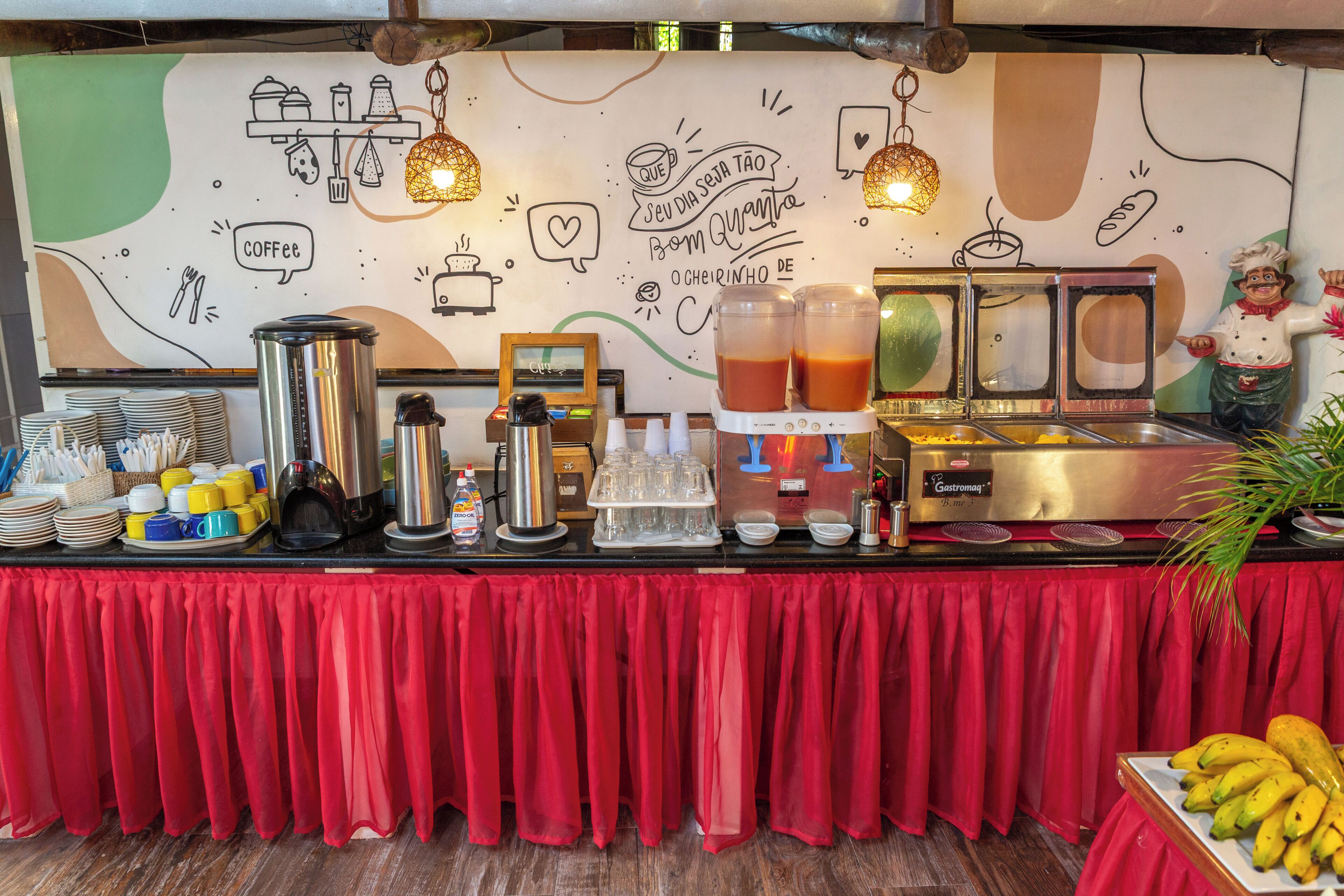 A buffet setup with a coffee station, a fruit display, and a wall with doodle-style drawings.