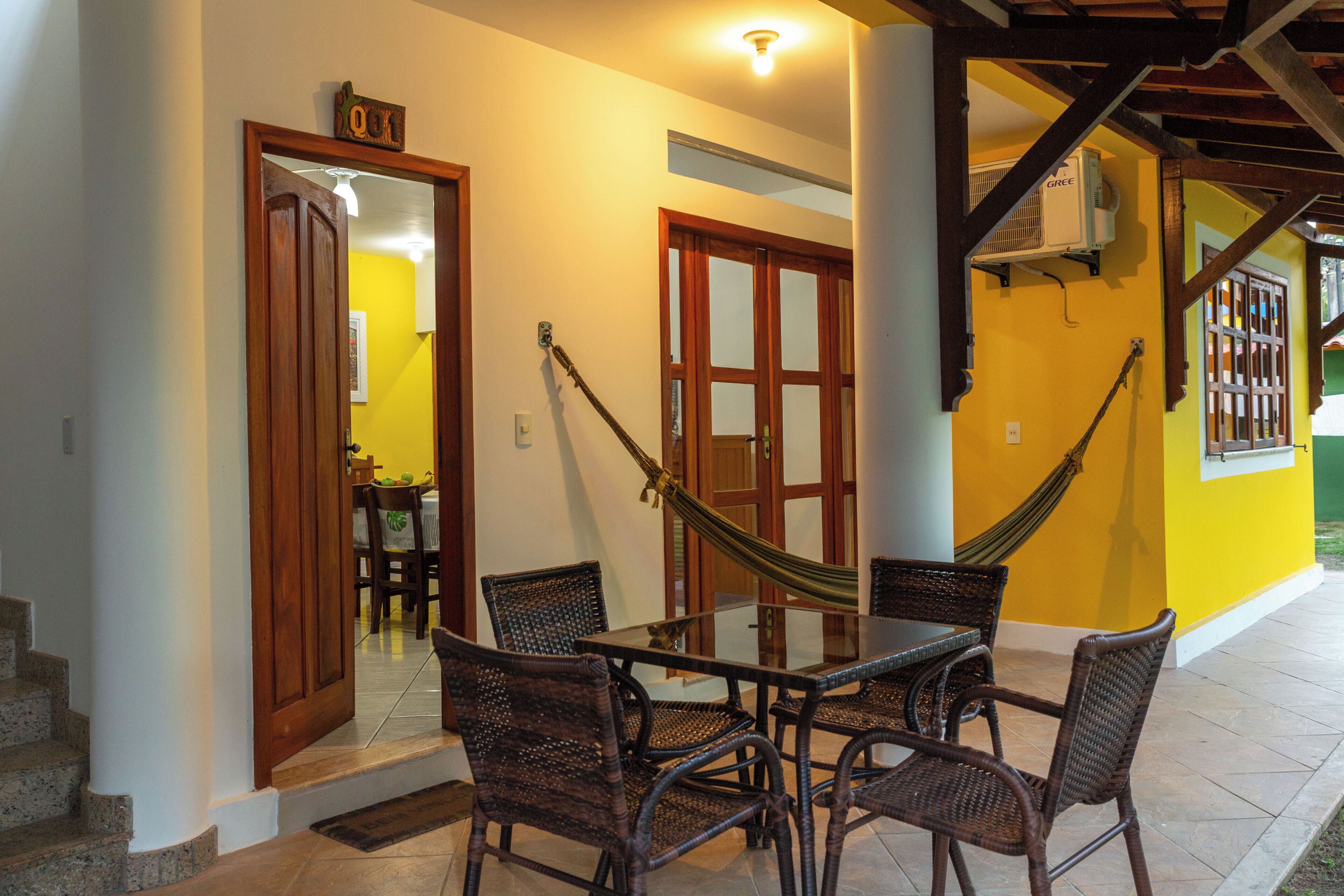 A dining area with a glass table and wicker chairs, a hammock, and a staircase leading to an upper level.