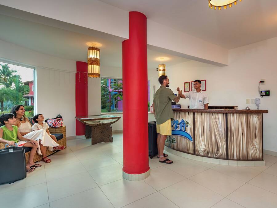 Uma área de recepção com balcão, um pilar vermelho grande e uma área de estar com uma mesa.