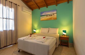 A hotel room with a bed, a painting of a beach scene, and a nightstand with a lamp. - Capoeira Village (Porto Seguro)