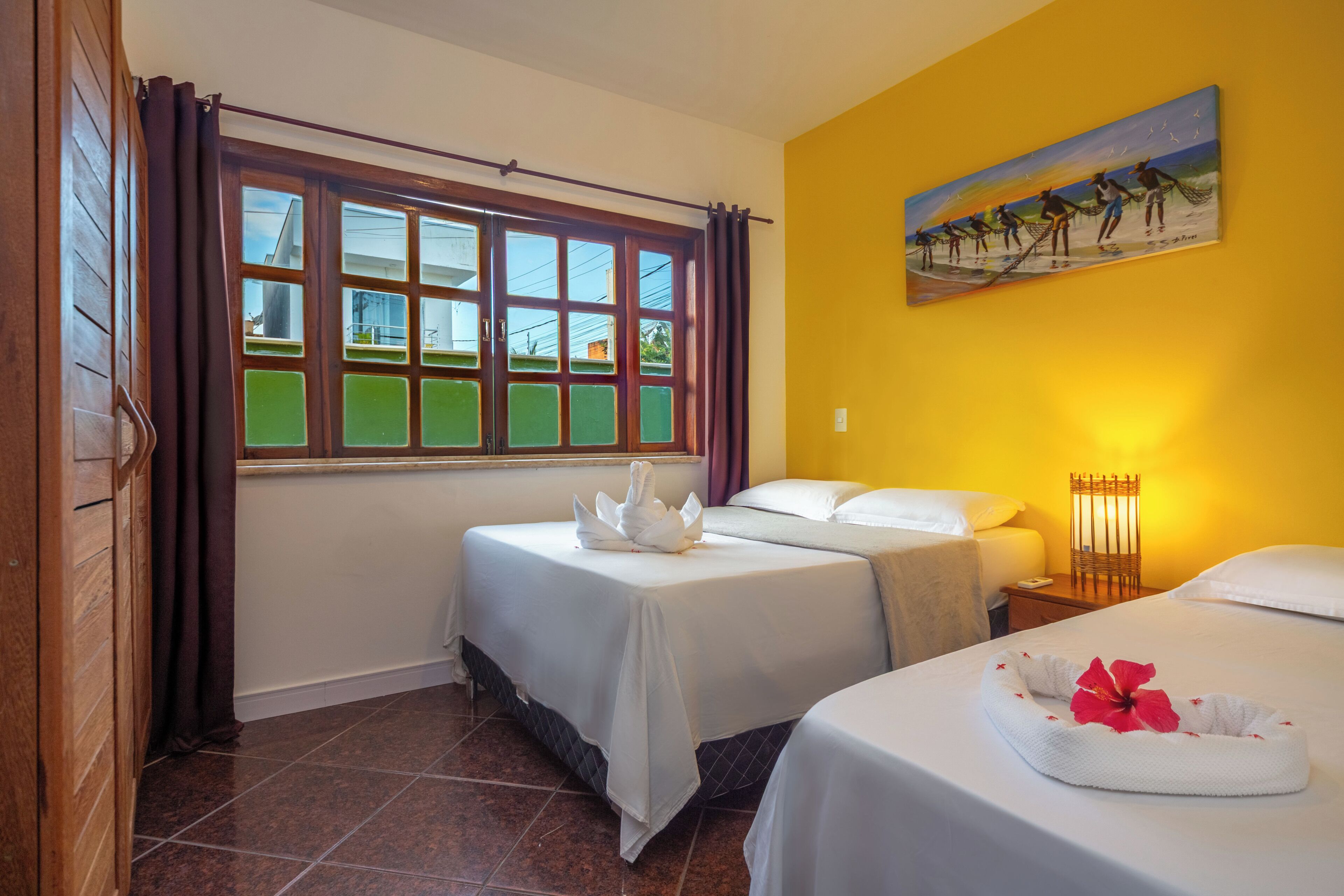 Quarto de hotel com duas camas, janela com cortinas, um quadro na parede e mesa de cabeceira com abajur.