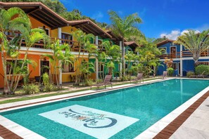 A swimming pool with a tiled design, surrounded by palm trees and buildings with balconies. - Capoeira Village (Porto Seguro)