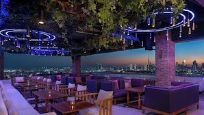 Un bar situé sur un toit, avec des places assises, une vue sur la ville et des guirlandes lumineuses.