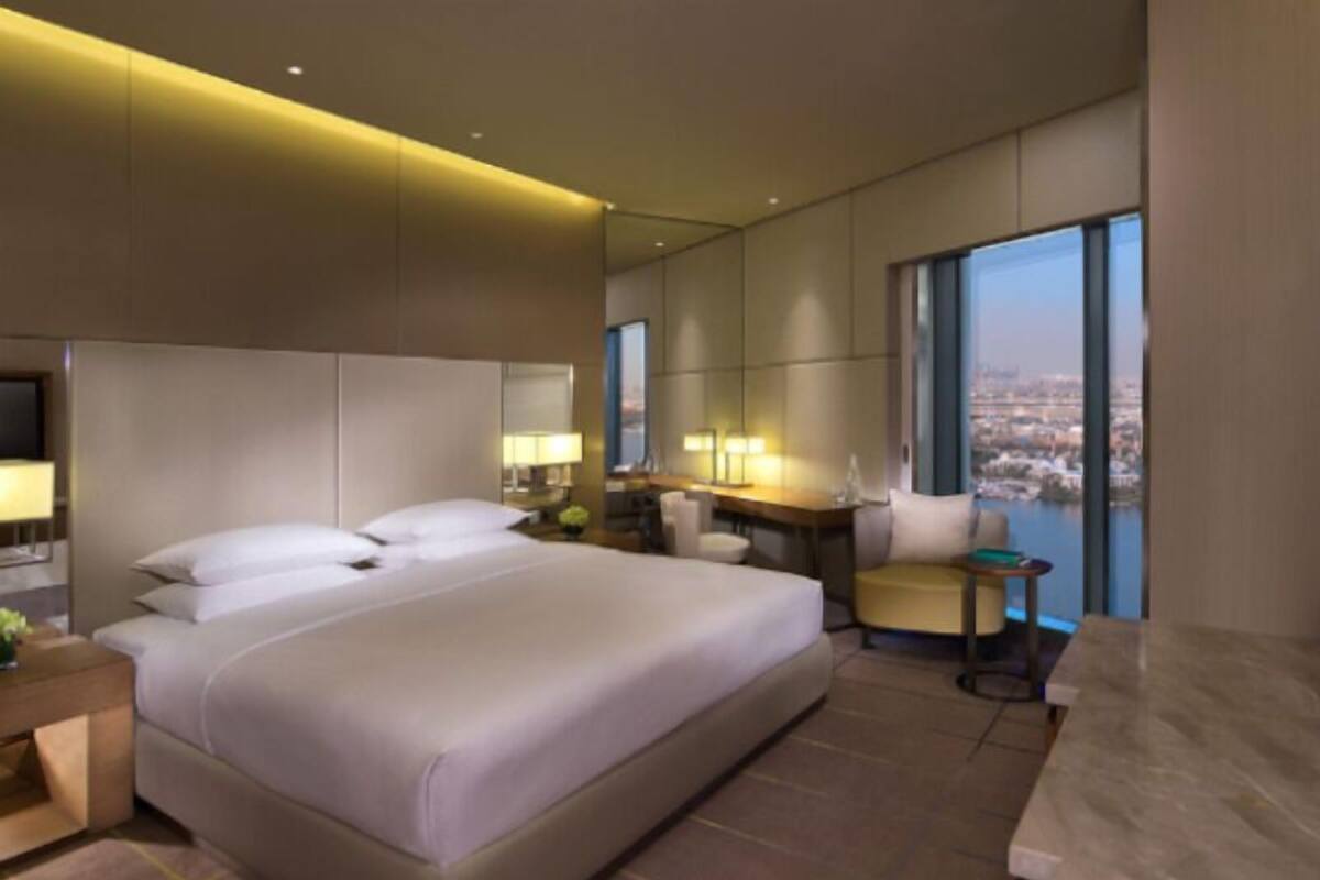 Habitación de hotel moderna con una cama grande, un escritorio y vistas a un paisaje urbano.