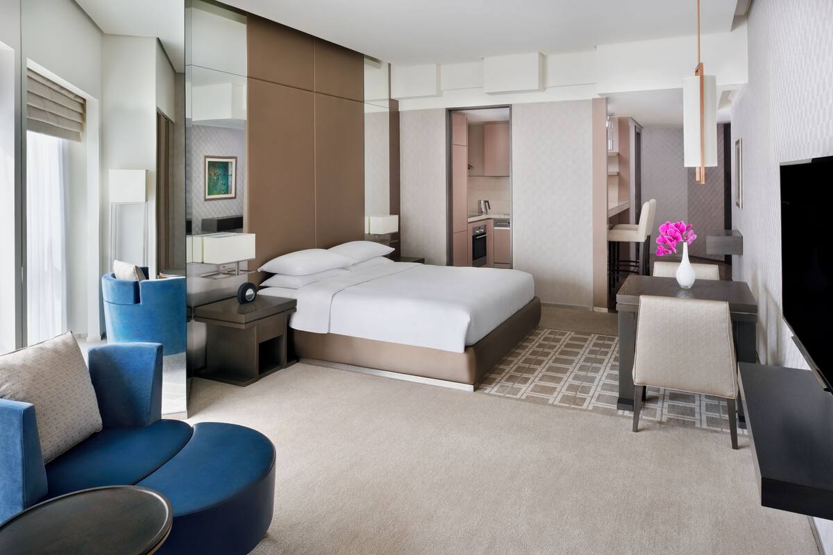 Una habitación de hotel moderna con una cama grande, una zona de estar con un sofá azul, una mesita y un escritorio.