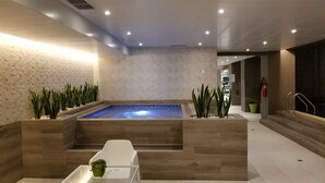 Uma área de spa moderna com uma banheira de hidromassagem retangular, piso de madeira e plantas decorativas.