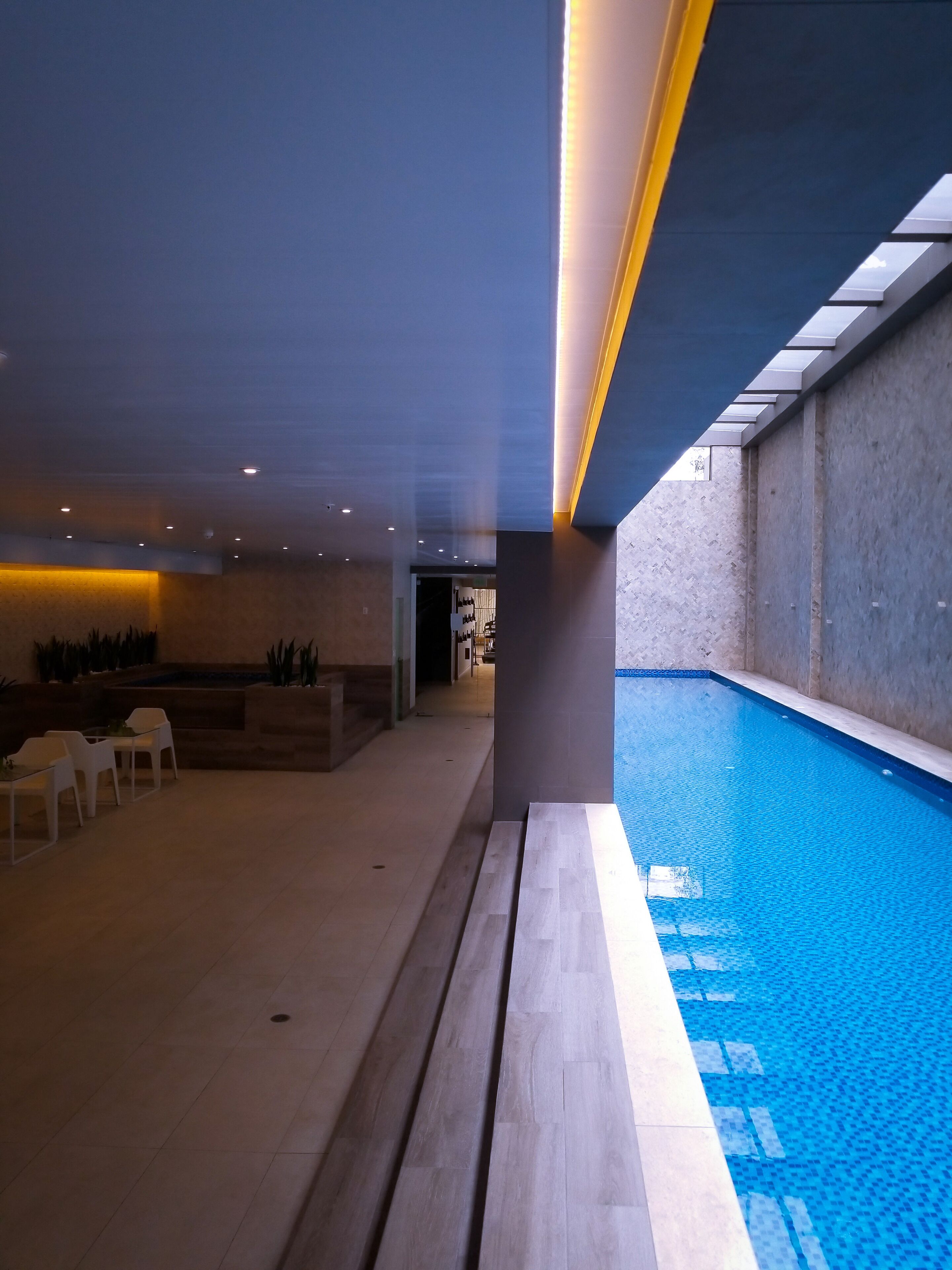 A modern indoor pool area with a clear view of the pool, a reception desk, and seating area.