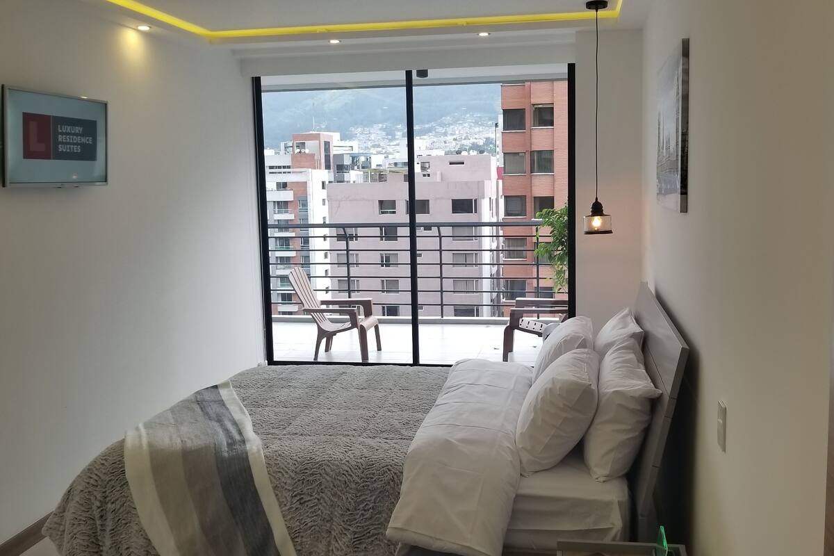 A bedroom with a bed, a view of the cityscape through a window, and a sign indicating luxury residence suites.