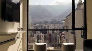 Varanda espaçosa com vista para a cidade, televisão de tela plana na parede e dois banquinhos redondos.