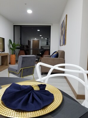 Una sala de estar moderna con comedor, que incluye un sofá, sillas, un televisor y una mesa de comedor con mantel individual.