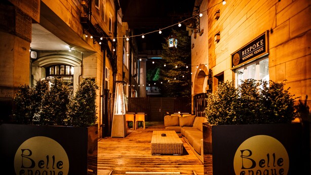 Un espacio al aire libre con piso de madera, un sofá y una mesa. Hay dos carteles con el texto "Belle époque".