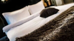 Una cama con ropa de cama blanca y un plaid suave oscuro.