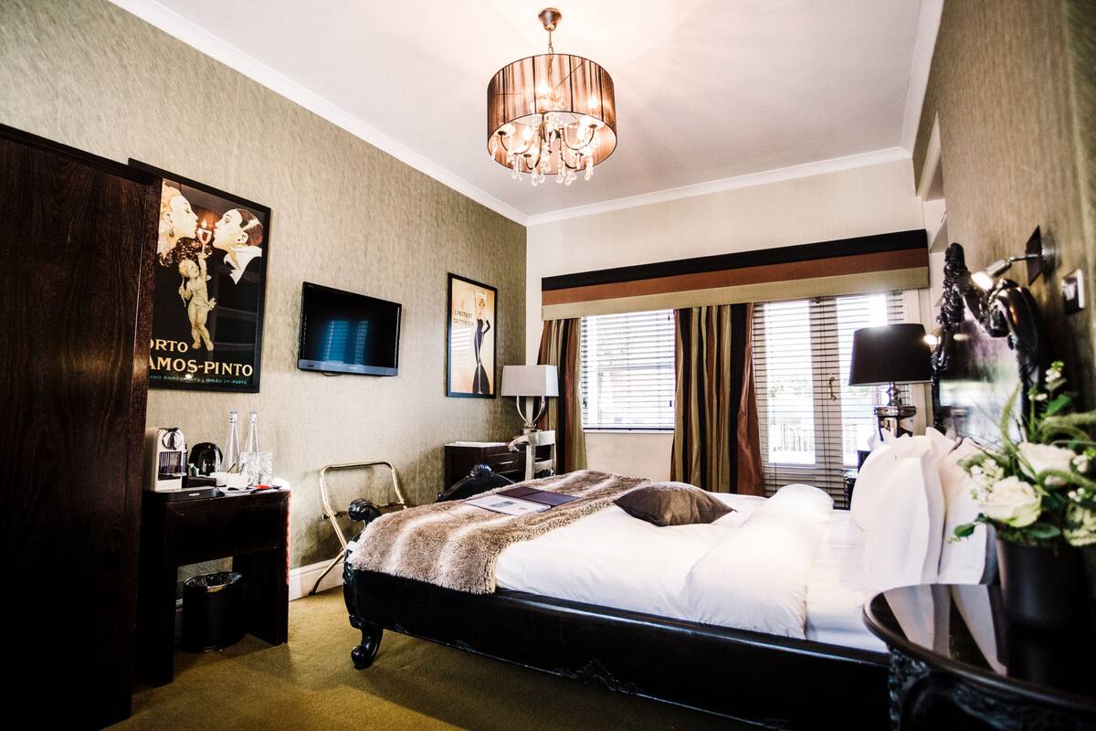 A hotel room with a large bed, a desk with a chair, a television, and a chandelier.
