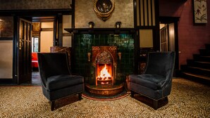 Una habitación con chimenea, dos sillones, un espejo y suelo estampado.