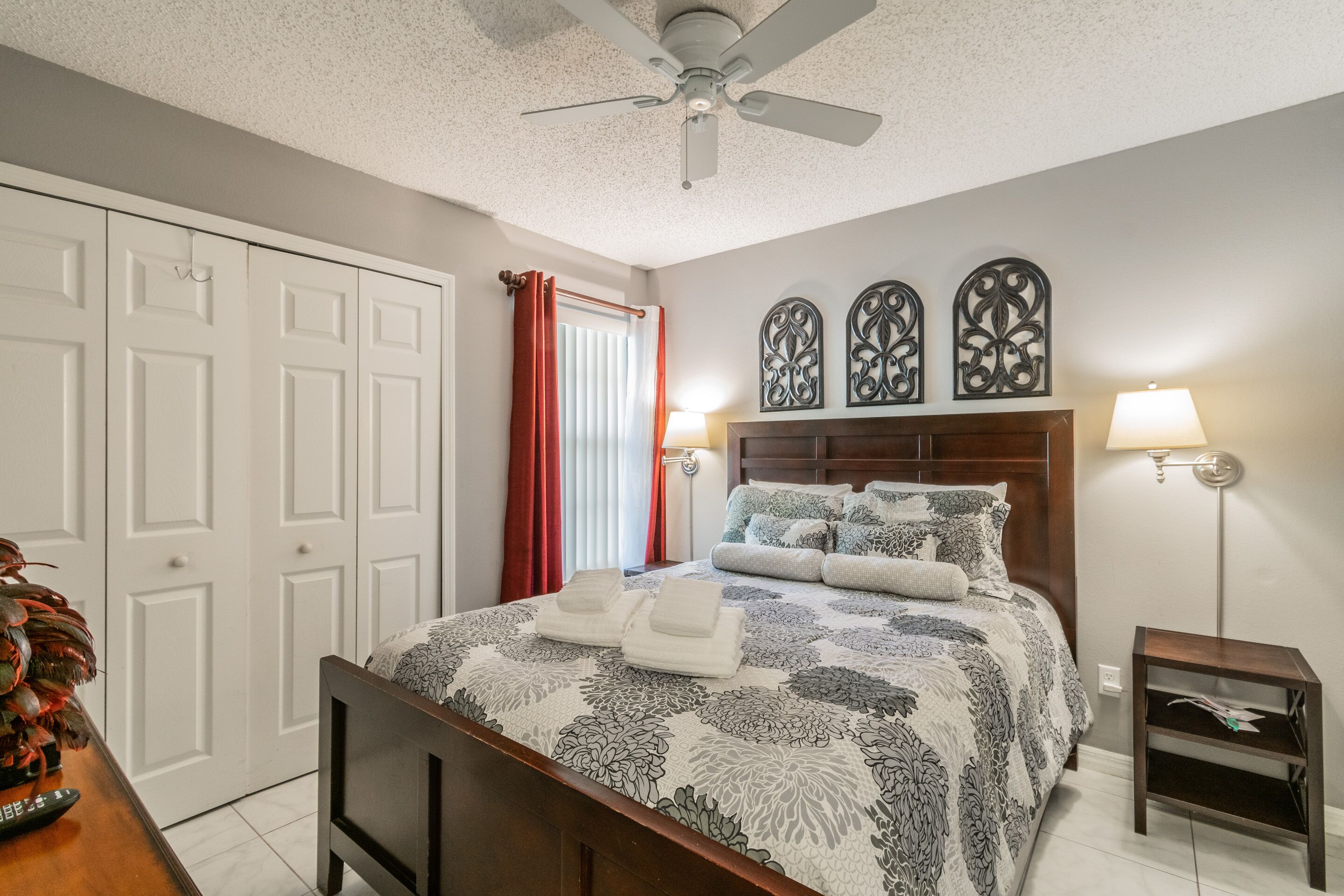 A bedroom with a bed, bedside lamps, a ceiling fan, and a door.