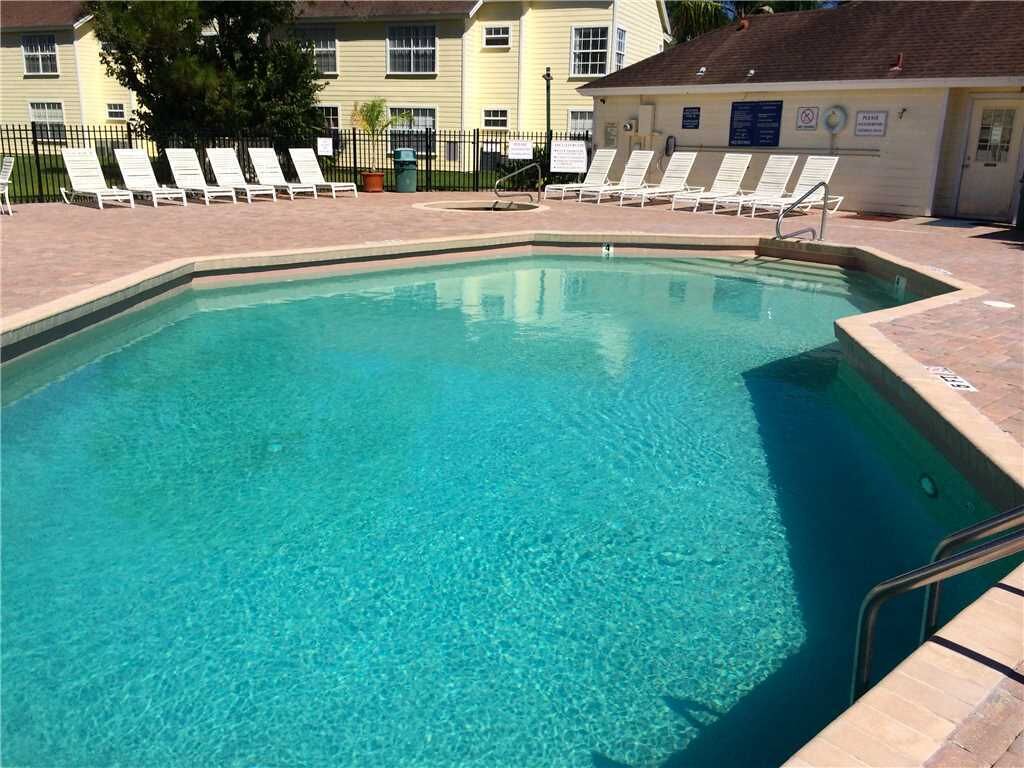 A clear swimming pool with lounge chairs and a building in the background.