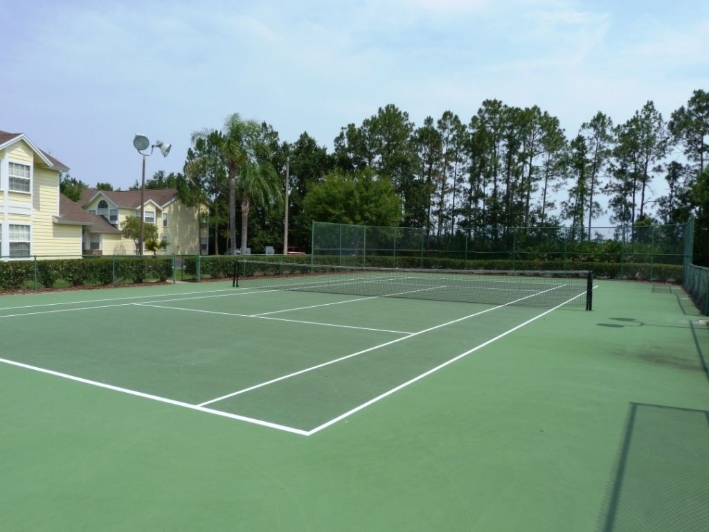 A tennis court with a net, surrounded by a fence and trees.
