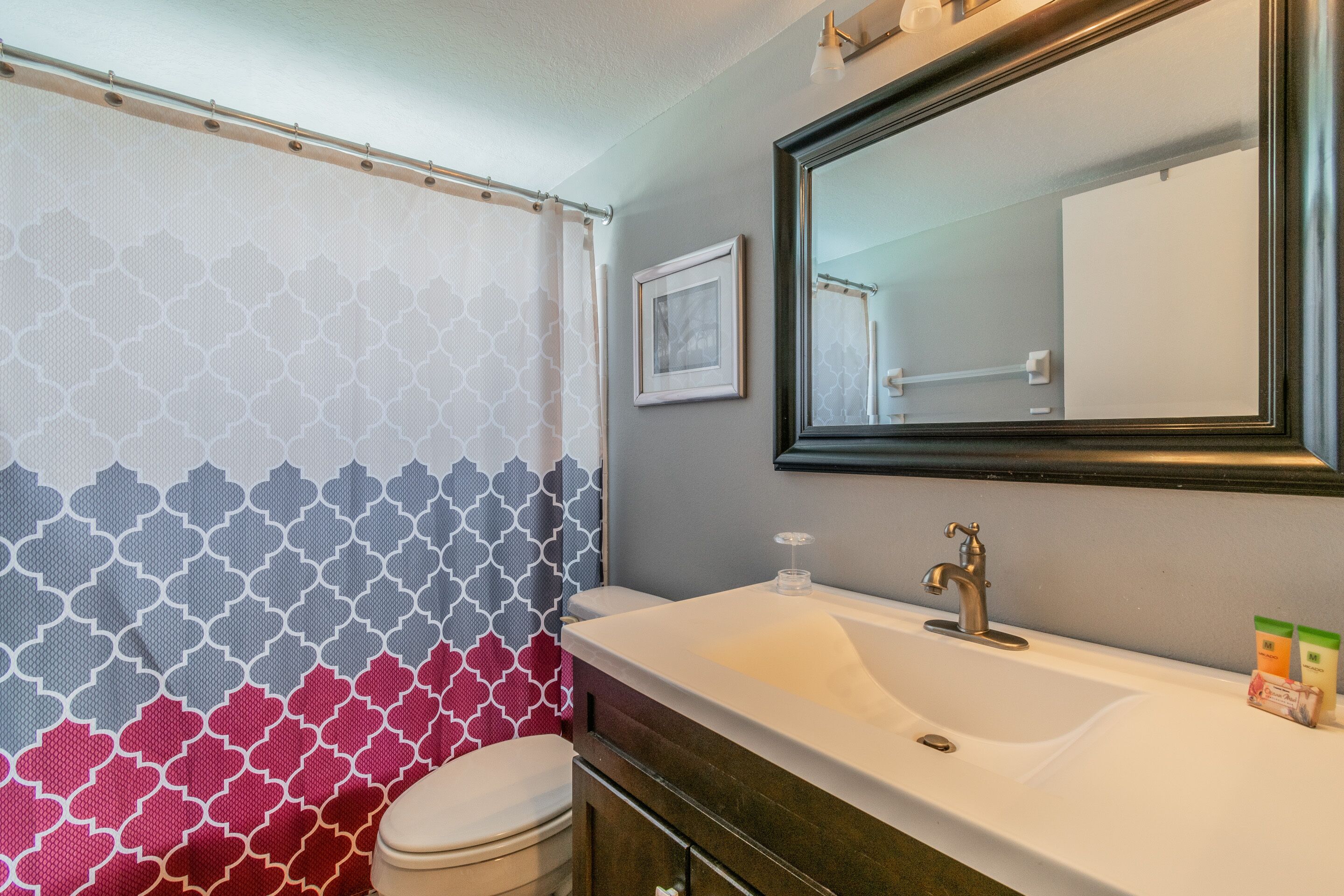 A bathroom with a patterned shower curtain, a sink with a mirror, and toiletries on the counter.