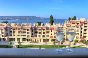 A hotel with a view of the sea, two glasses of white wine on the balcony, and a courtyard with trees. - Waterfront Sea Star 2 bedroom Apartment (Varna)