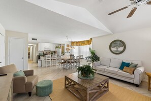 A spacious living area with a sofa, coffee table, and dining table. There is a kitchen in the background with white cabinets and a dining area. - ​Near Theme Parks! 4 BR's, Sleeps 10! Gorgeous Home, Pool, Patio! (Kissimmee)