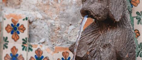 A stone fountain with water flowing, set against a wall with colorful floral tiles.