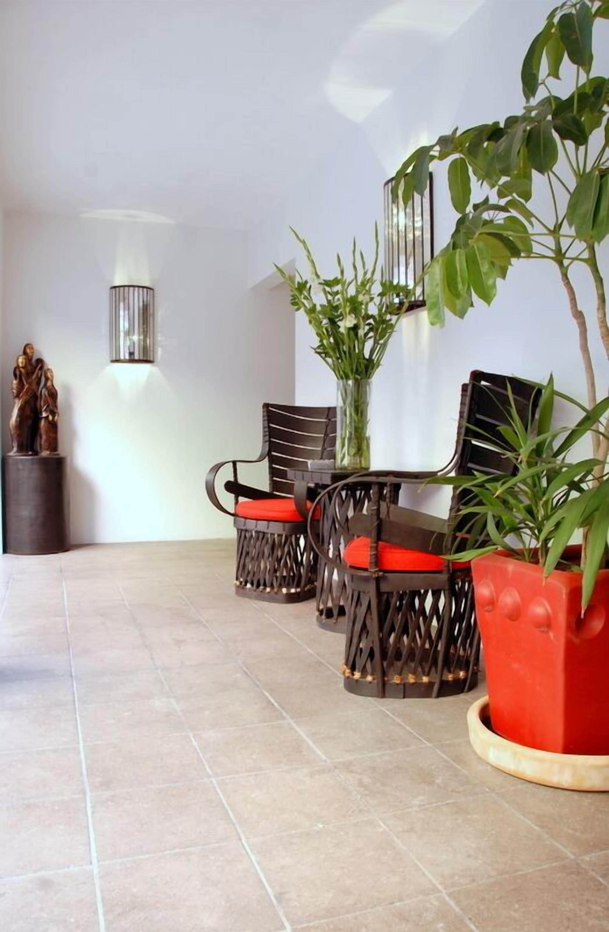 A room with a tiled floor, two wicker chairs with red cushions, a potted plant, and a wall-mounted light fixture.