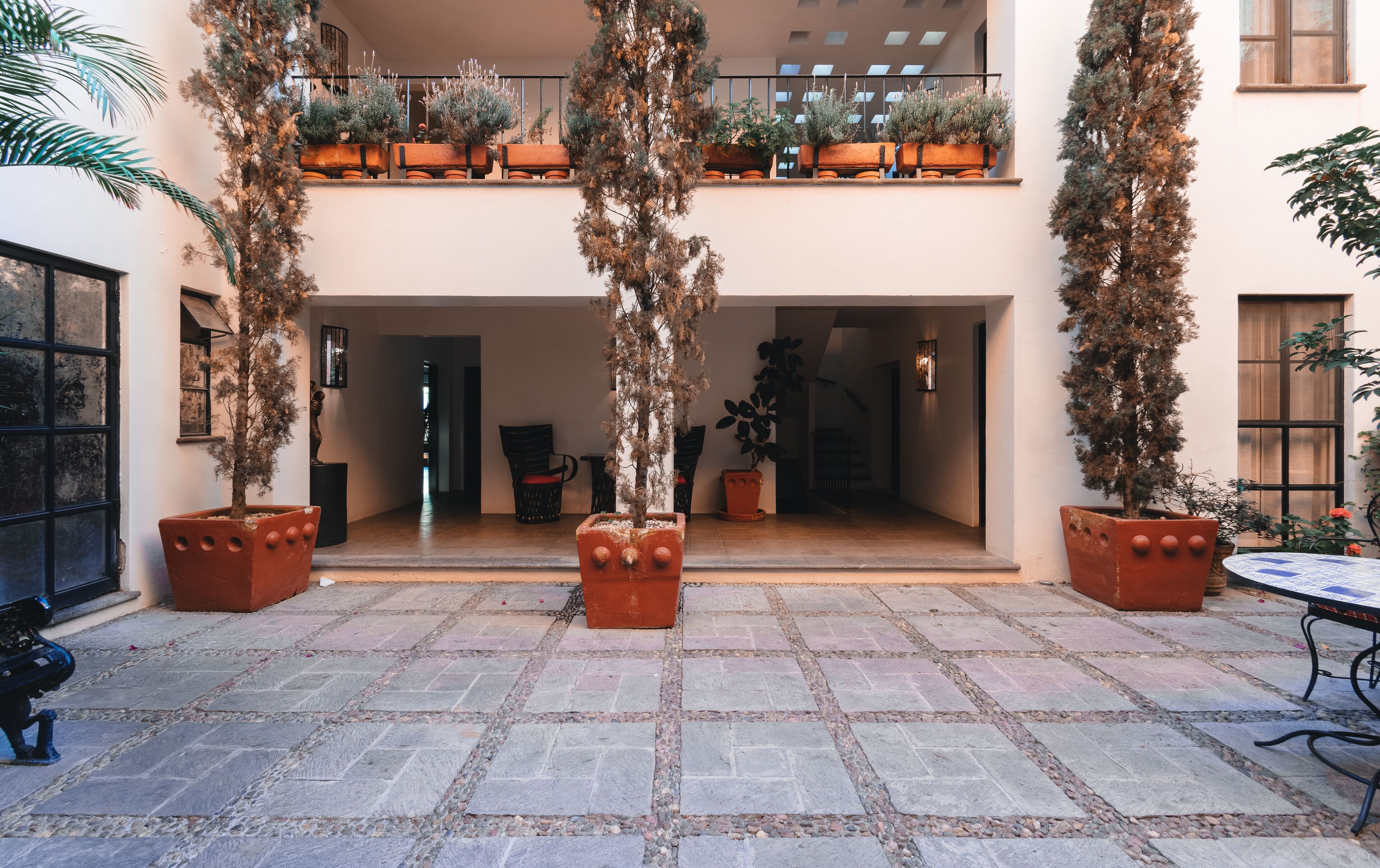 A courtyard with a tiled floor, potted plants, a table, and chairs.