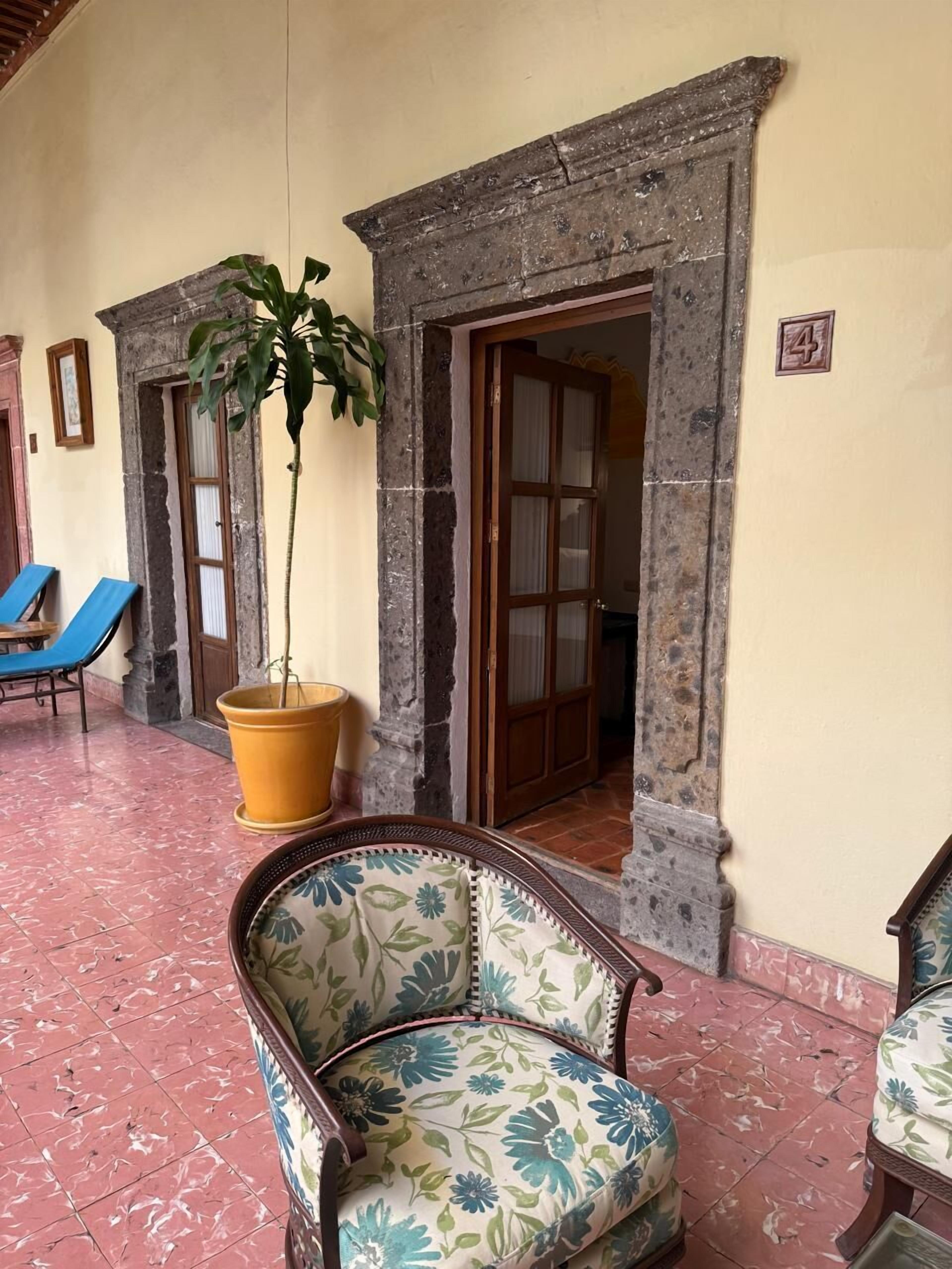 Una habitación con una silla, una planta en maceta y una puerta que da a otra estancia.