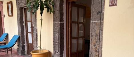 Una habitación con una silla, una planta en maceta y una puerta que da a otra estancia.
